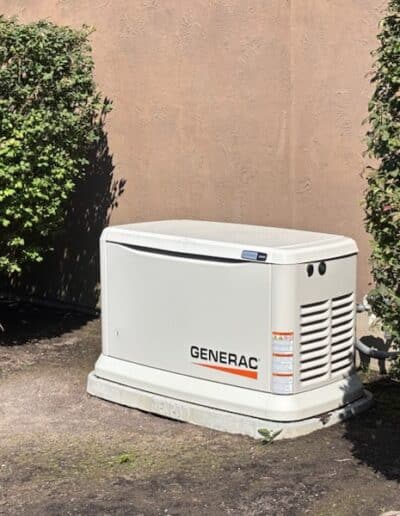 Generac residential backup generator installed between landscaping beside a home
